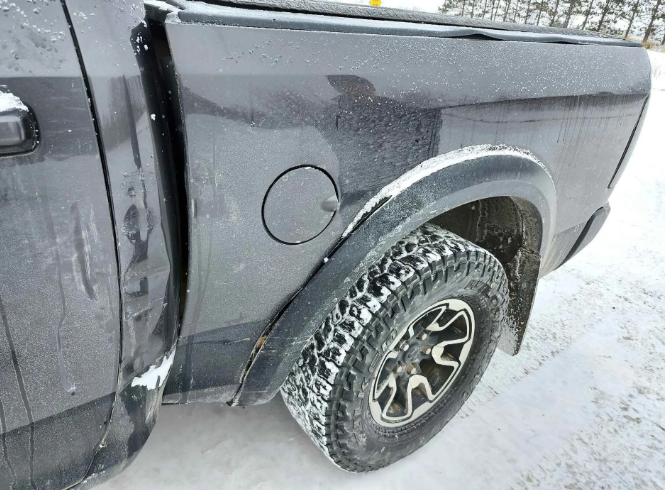 Gray pickup truck rear wheel in snowy conditions, showing a dented side panel and wheel arch