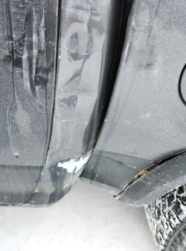 Close-up of a black vehicle’s side panel with white scrapes and a damaged wheel arch near the tire