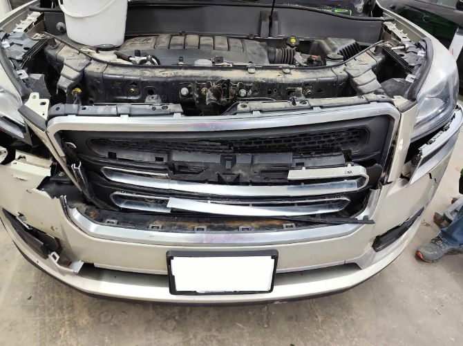 Front view of a silver SUV with a damaged front grille and bumper in a garage