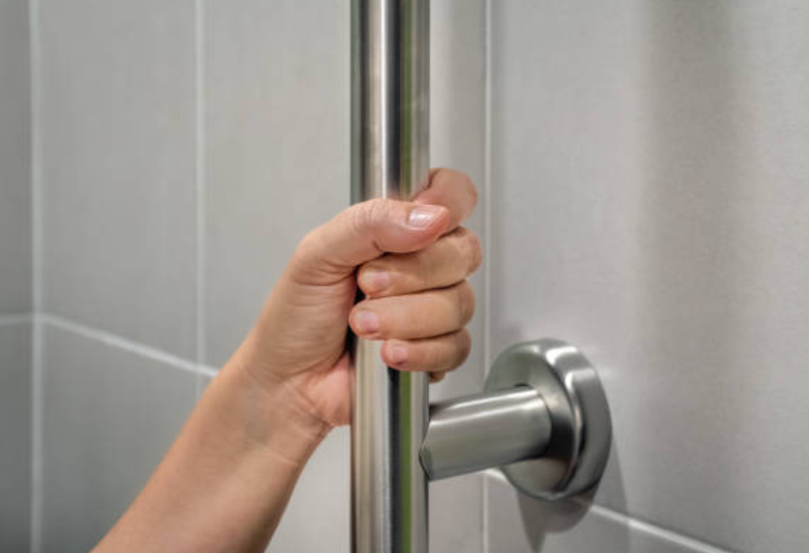 A person is holding onto a stainless steel railing in a bathroom.