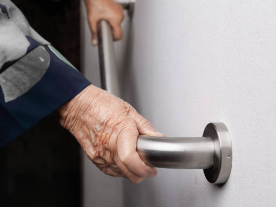 An elderly woman is holding onto a door handle.