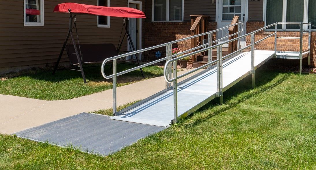 A wheelchair ramp is sitting in the grass in front of a house.