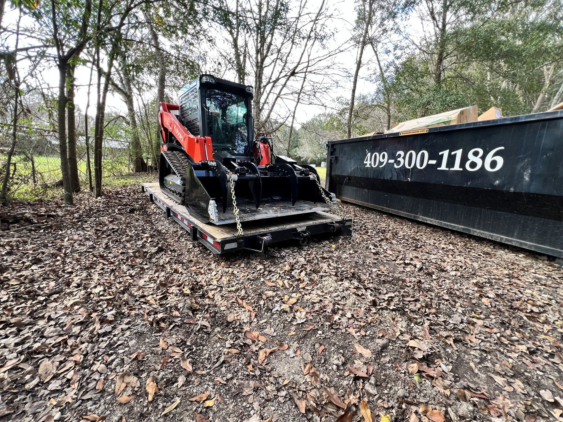 Orange Kubota track loader with grapple bucket on a trailer.