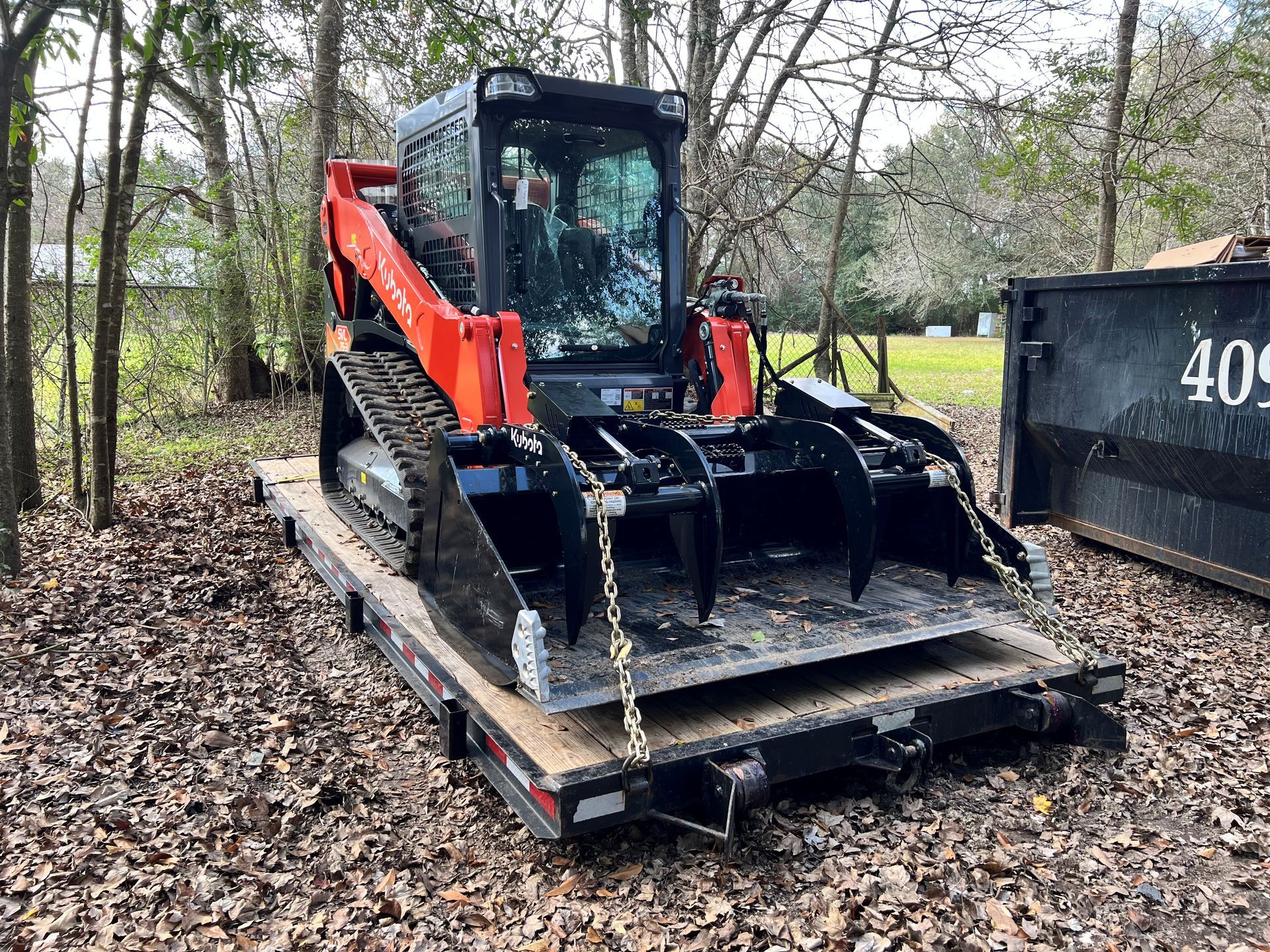 Orange Kubota track loader with grapple bucket on a trailer.
