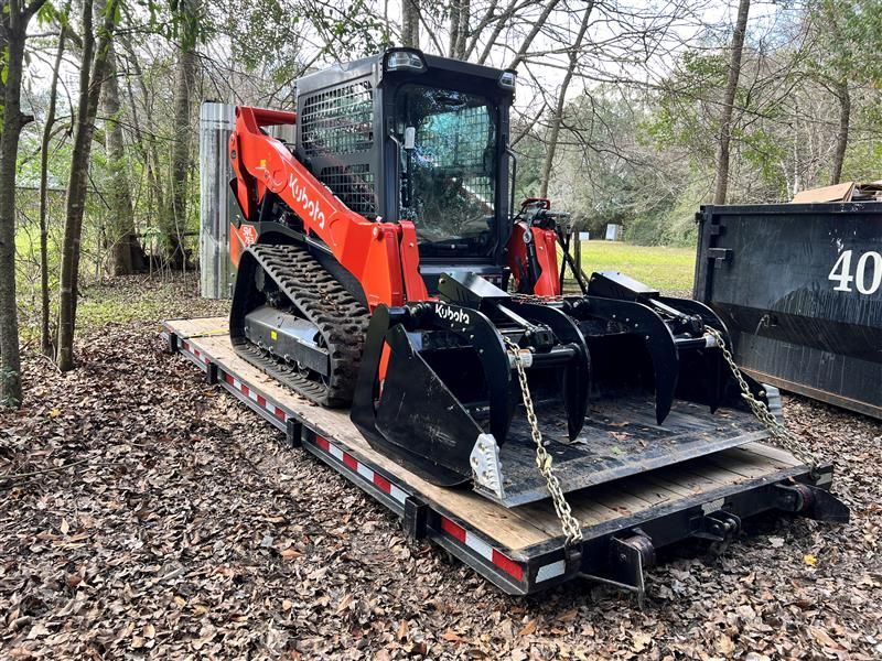 Orange Kubota track loader with grapple bucket on a trailer.