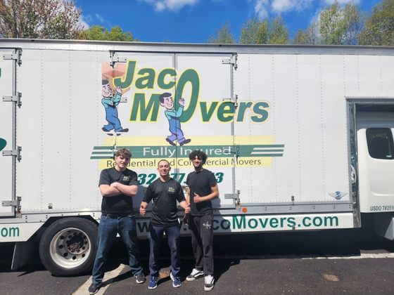 Three movers posing in front of a white Jac Movers truck on a sunny day.