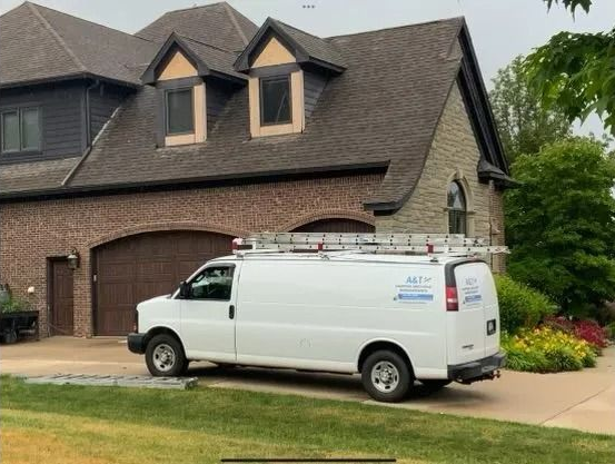 White van with ladder parked in front of a house. Brick, stone, and brown roof.