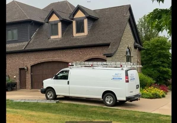 White service van parked in front of a brick and stone house. Ladder on top.