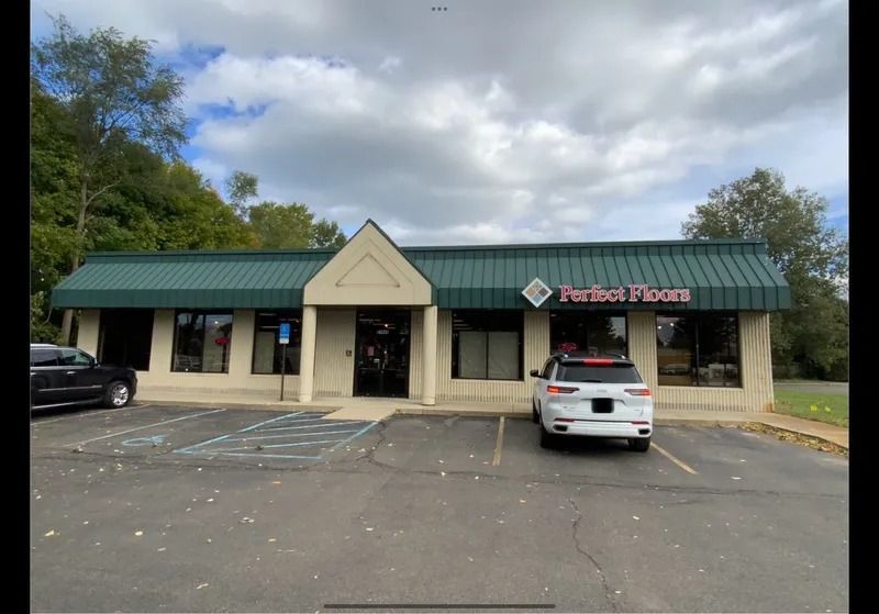 Exterior of Perfect Floors store with green awning, beige facade, and parked vehicles.