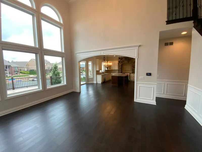 Interior view: A large, open living space with dark wood floors, large windows, and a view of a kitchen.