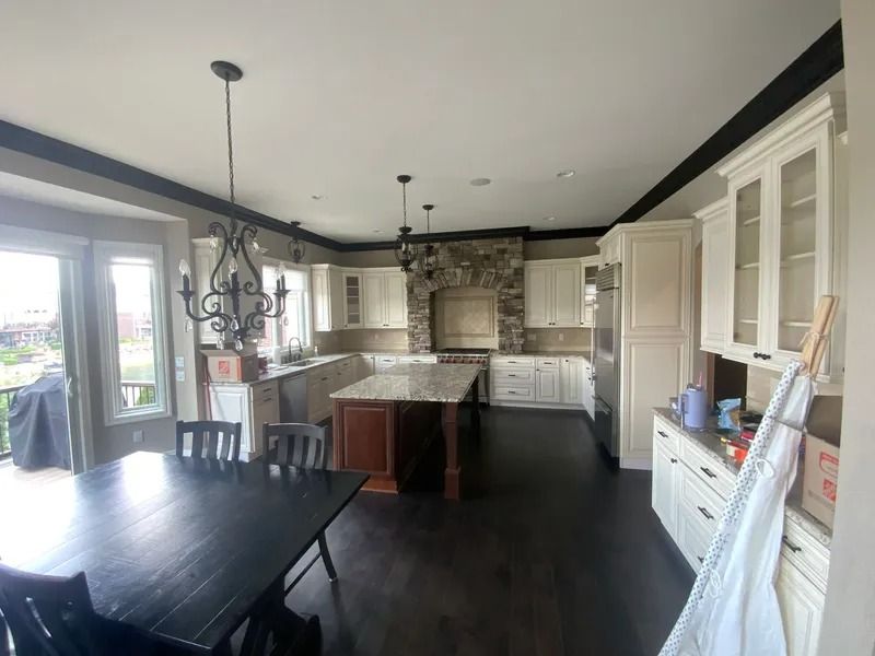 Spacious kitchen with dark wood floors, white cabinets, and a stone accent wall. A dark island sits center.