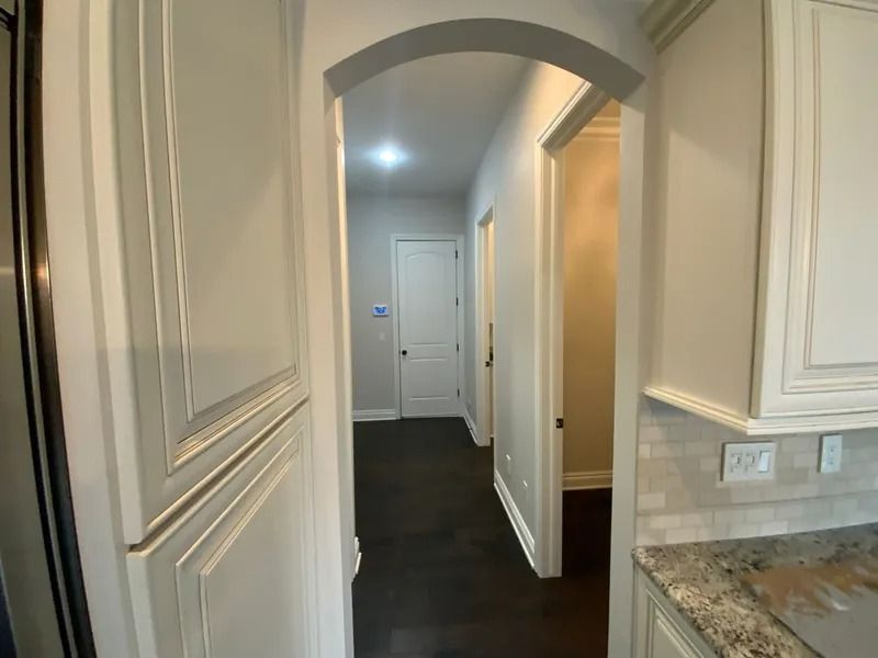 Hallway with dark flooring, archway, and white trim. Doors are visible in the distance.
