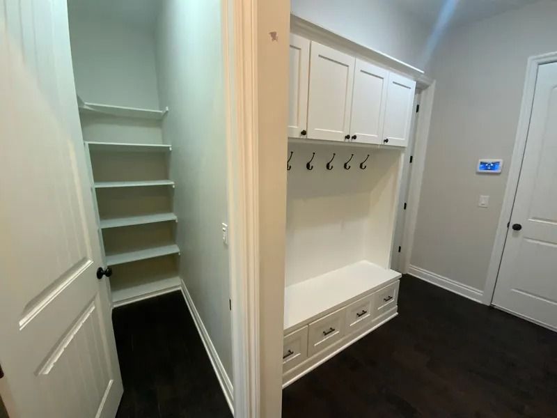 Hallway with white built-in storage: closet with shelves and hooks above bench with drawers. Dark wood floor.