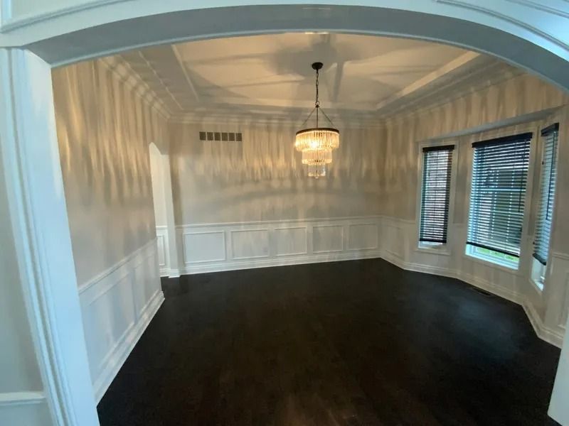 Empty dining room with dark wood floor, white paneled walls, and a chandelier.