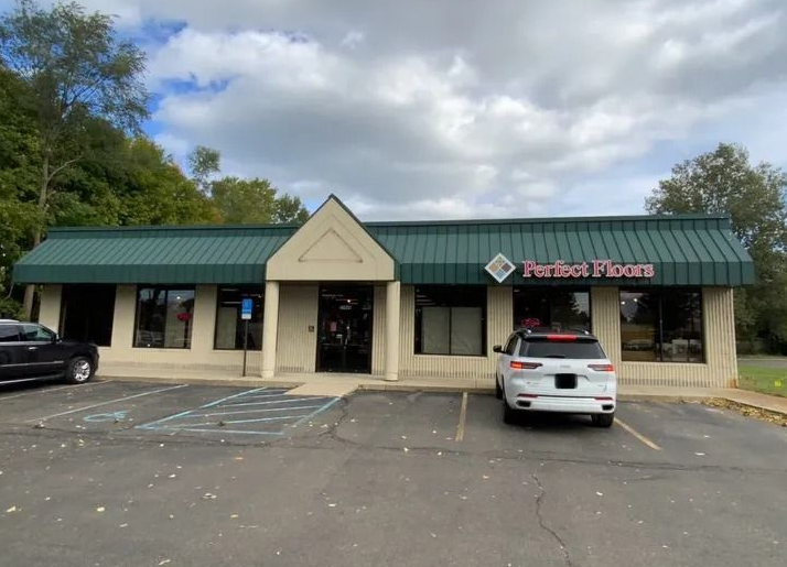 Exterior of "Perfect Floors" store, a beige building with a green awning. Cars parked out front.