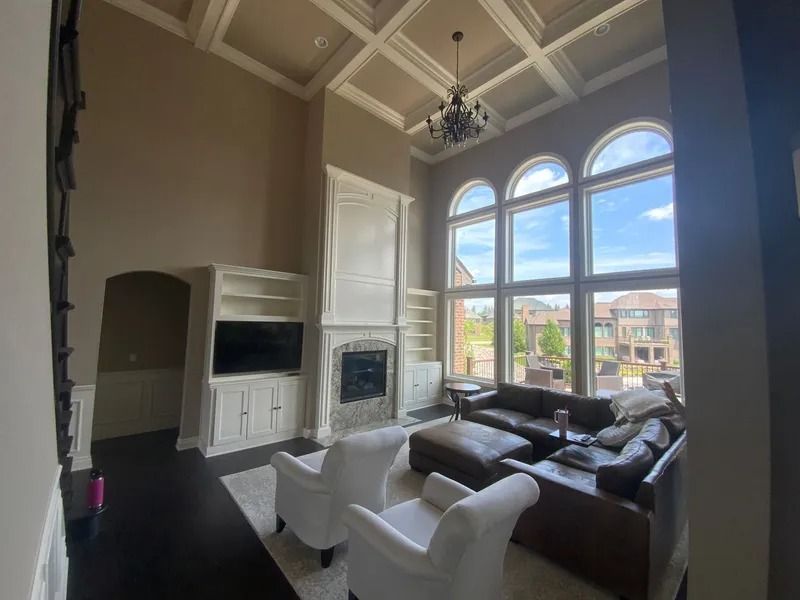 Spacious living room with high ceiling, large windows, fireplace, and two white armchairs.