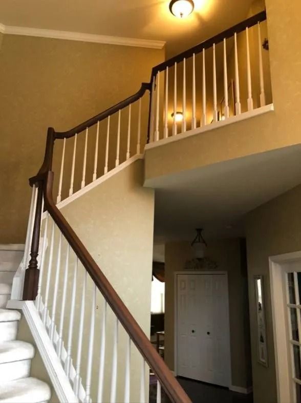Staircase with white balusters and brown banister, ascending to a second floor landing. Yellow walls.