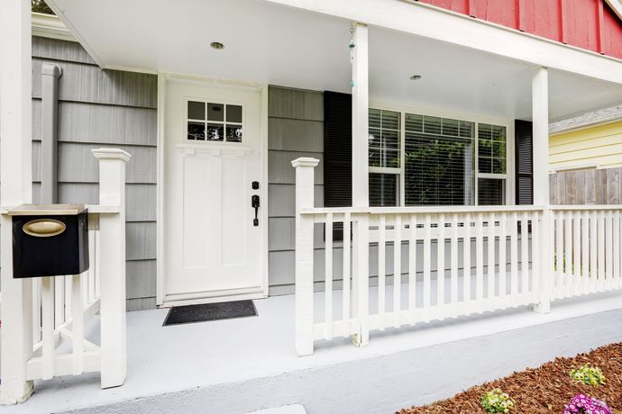 White front porch with mailbox, door, and railings. Grey siding on the house.