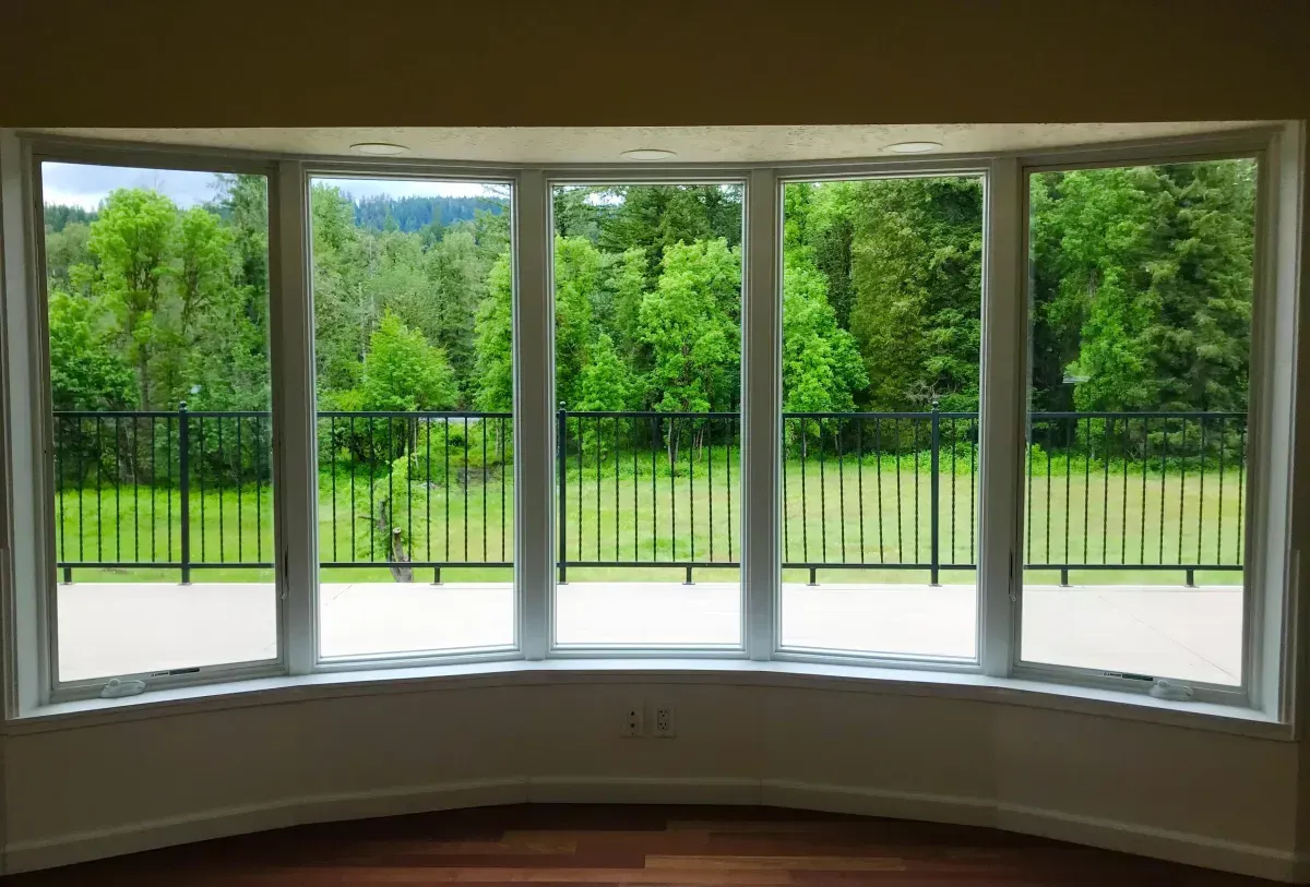 Bay window overlooking a lush green yard with a black fence.