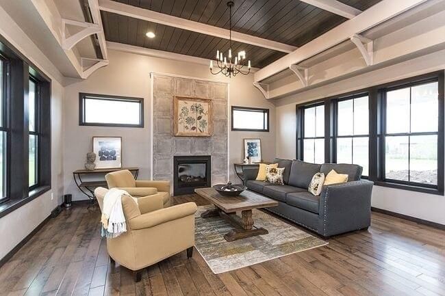Living room with wood floors, stone fireplace, and dark-framed windows; sofa, chairs, rug, and chandelier.