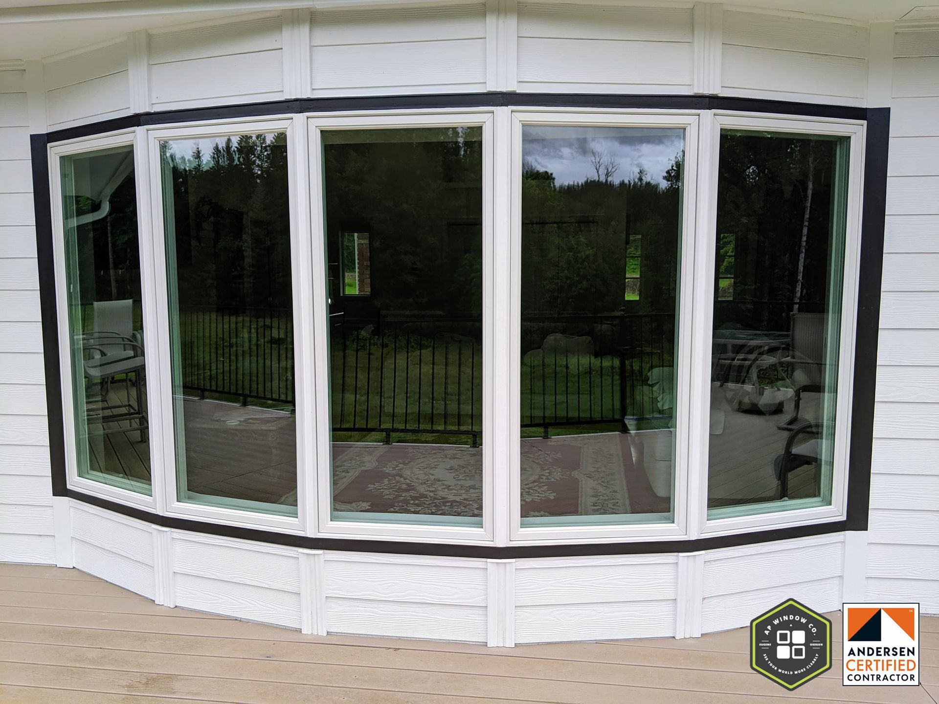 Bay window with white trim, dark framing, reflecting a backyard view.