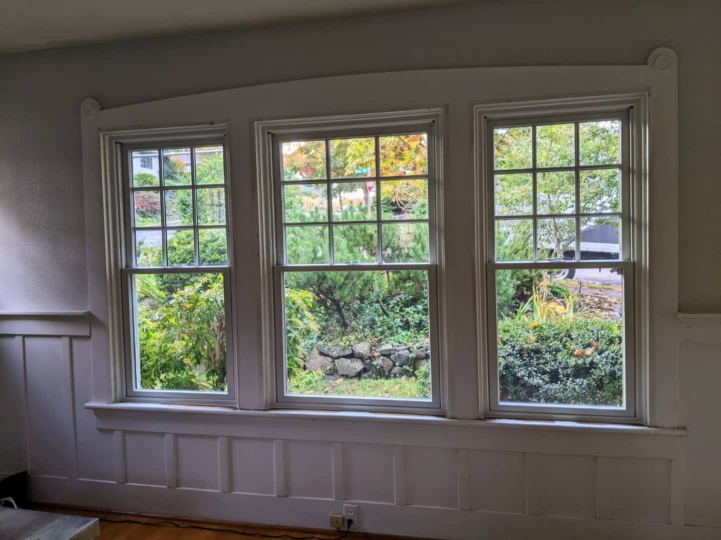 Triple-pane, white-framed windows overlooking a green, lush garden. White trim and paneling.