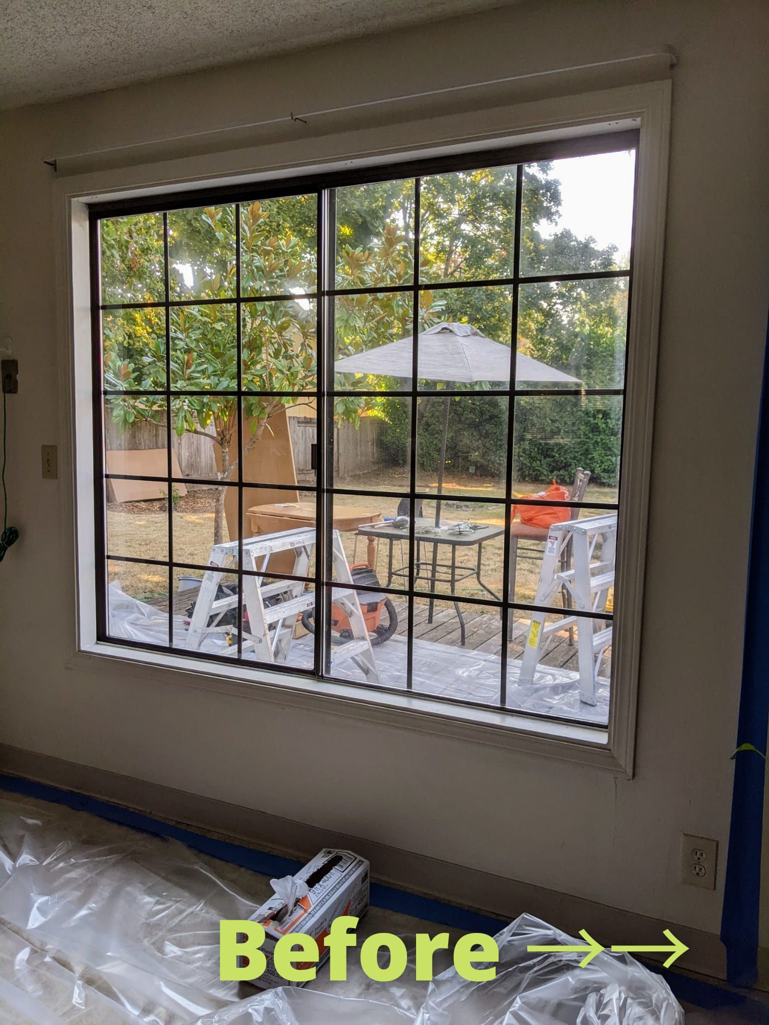 Window before renovation: black grid, white trim, backyard view with patio furniture.