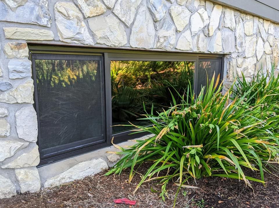 Window set into stone wall, with black frame, overlooking greenery.