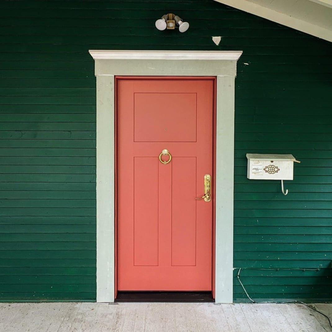 Red door framed in gray, on a green house. Mailbox on the right, light above the door.