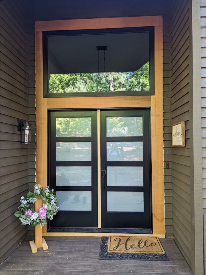 Modern entry with double black doors, large window, wood trim, and a 