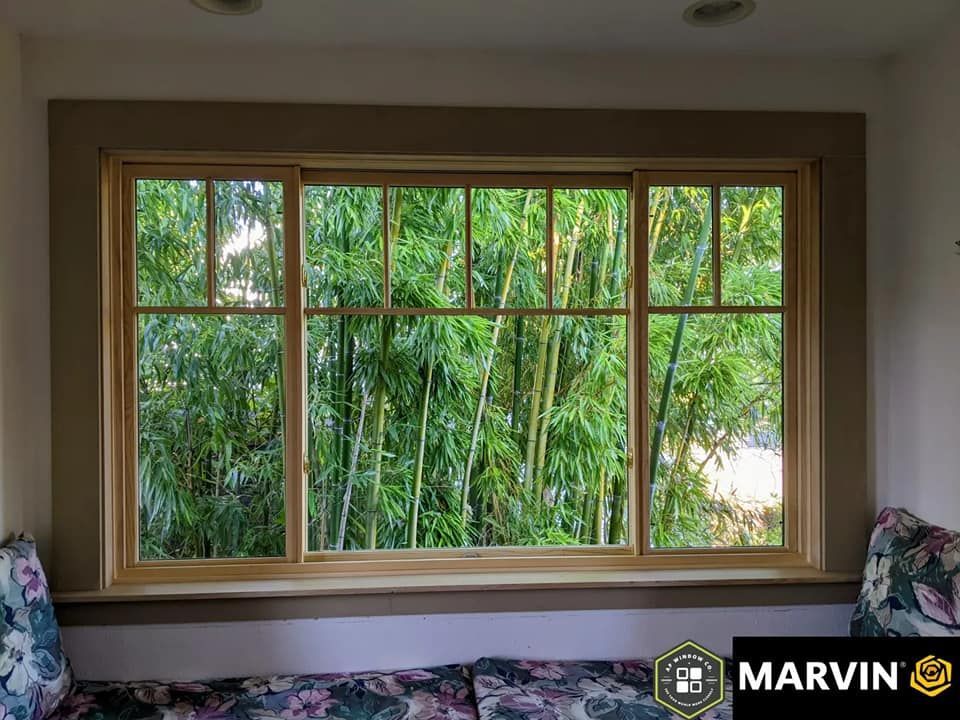 Large window with a view of bamboo trees, set in a wood frame with a window seat and decorative trim.