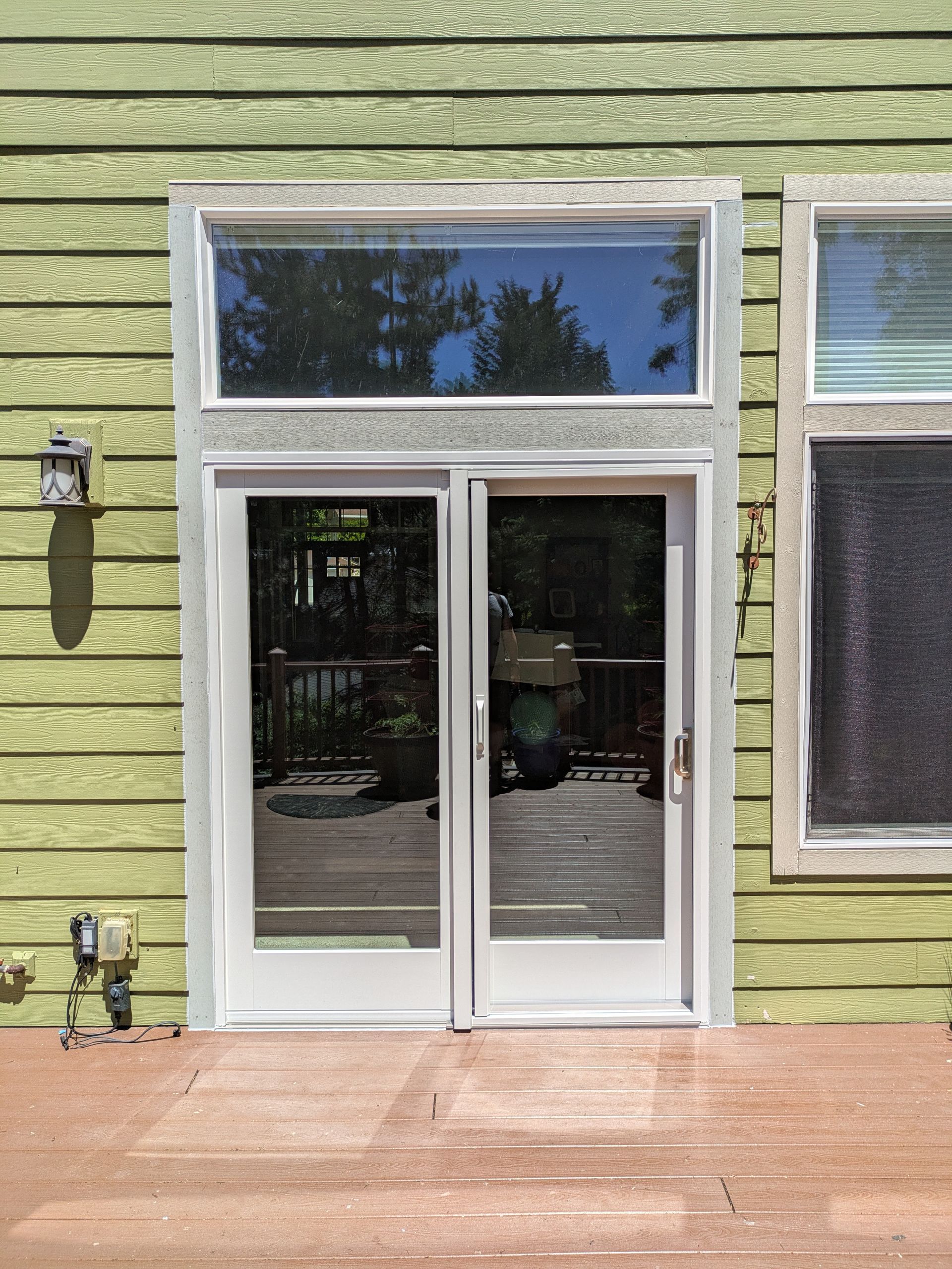 Double glass doors with a window above, set in green siding, opening onto a wooden deck.