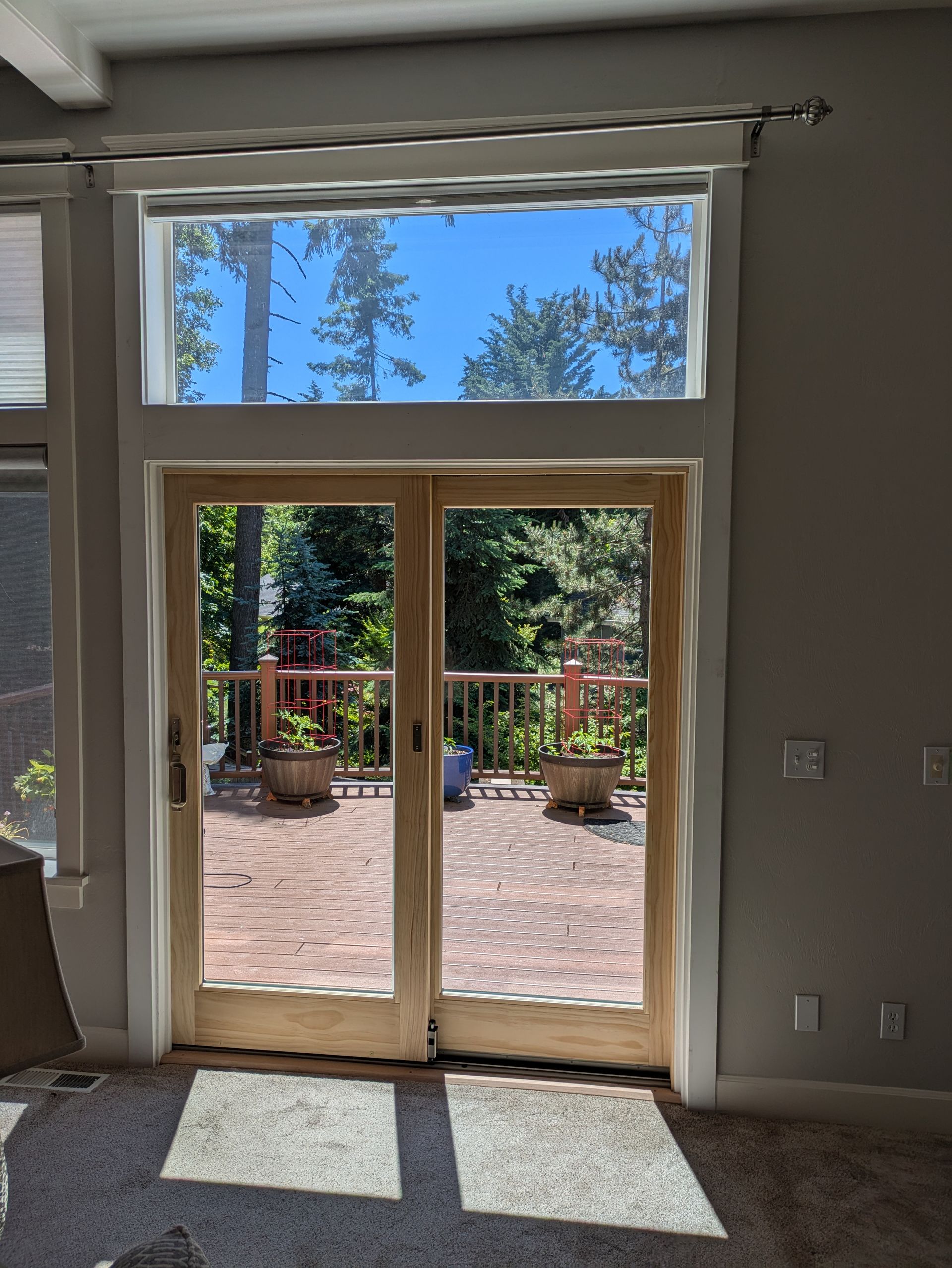 Glass doors open to a brick patio with potted plants and trees, beneath a clear, blue sky.