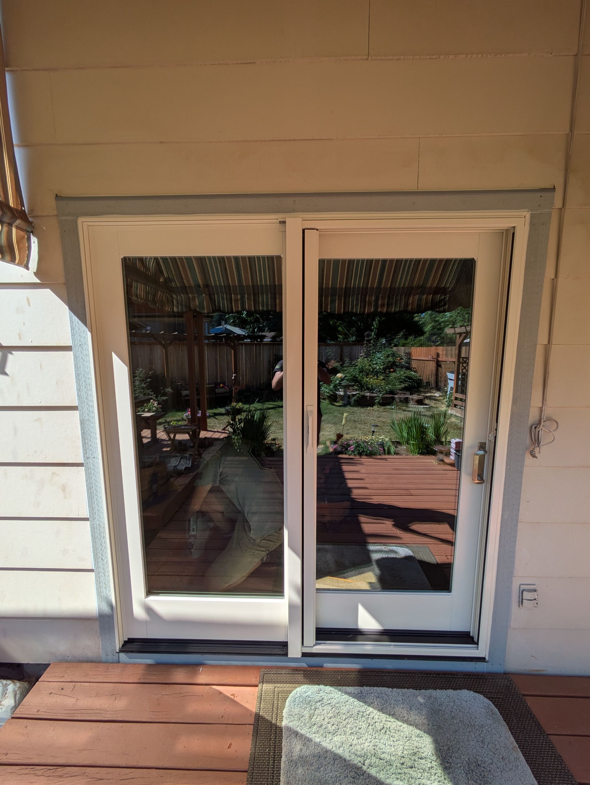 Sliding glass doors reflecting a backyard deck and garden, framed by white trim.