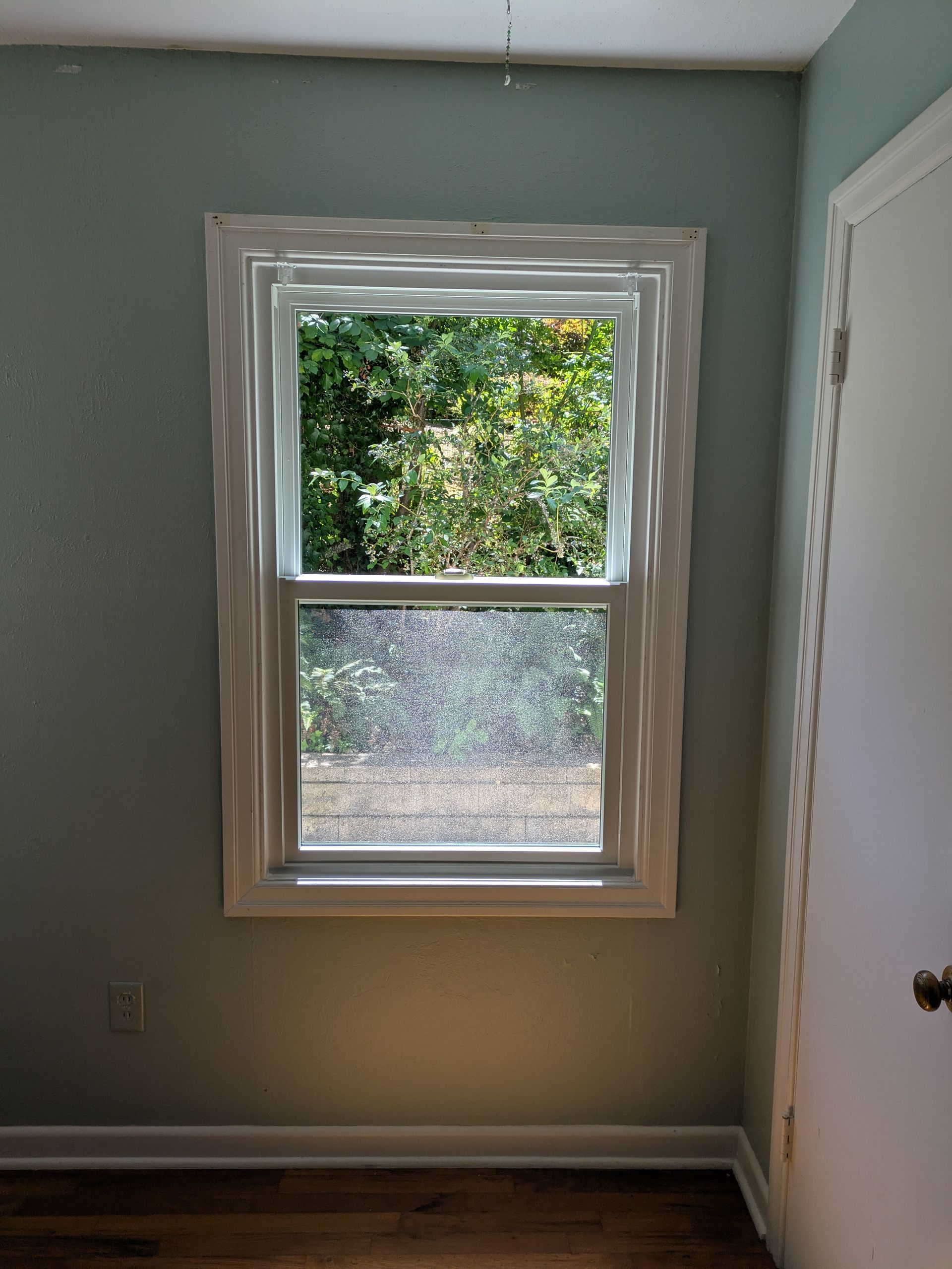 Window framed in white trim, looking out onto a green, tree-filled landscape. Blue-green walls.