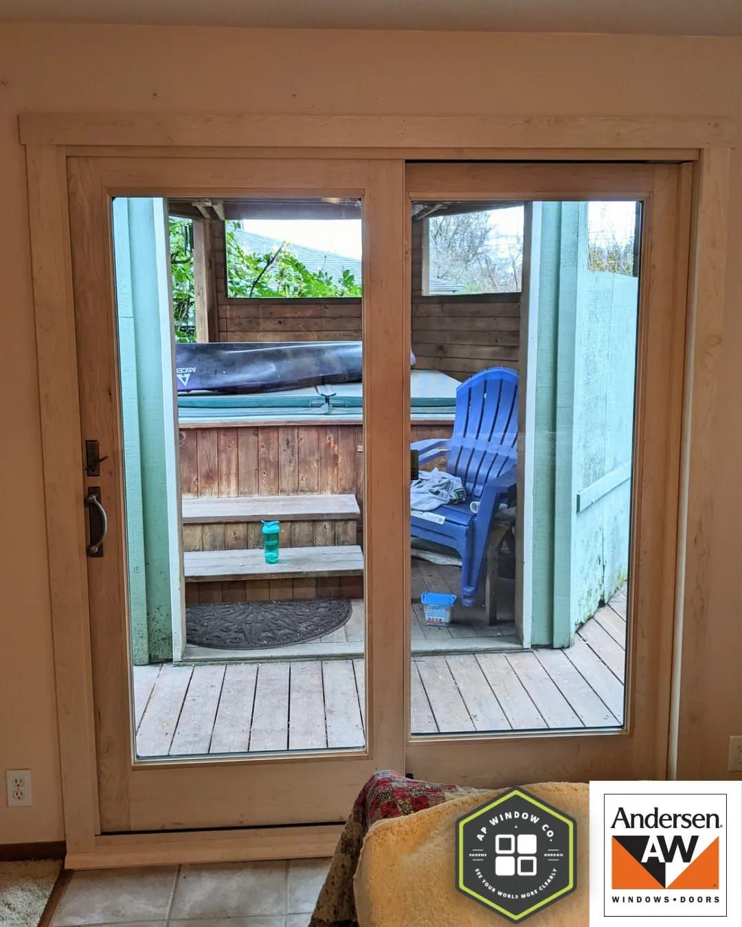 Sliding glass doors open to a hot tub on a wooden deck. A blue chair sits nearby.