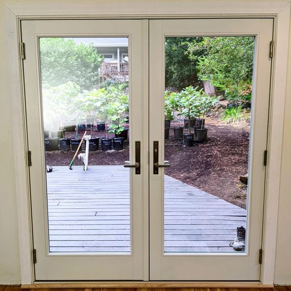Double white doors with glass panels looking onto a wooden deck and backyard with plants.