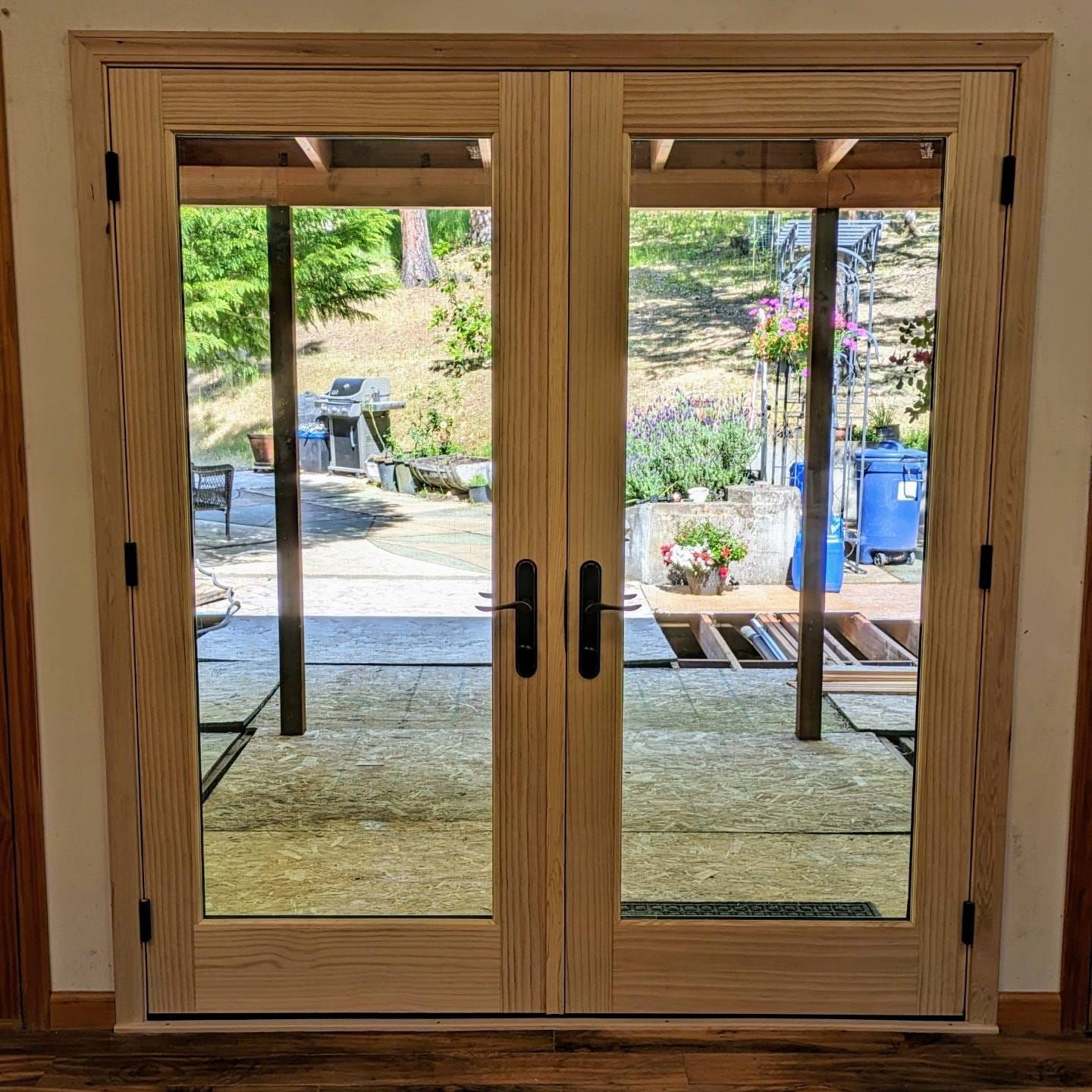 Double wooden doors with glass panes, black handles, and a view of a patio and garden.
