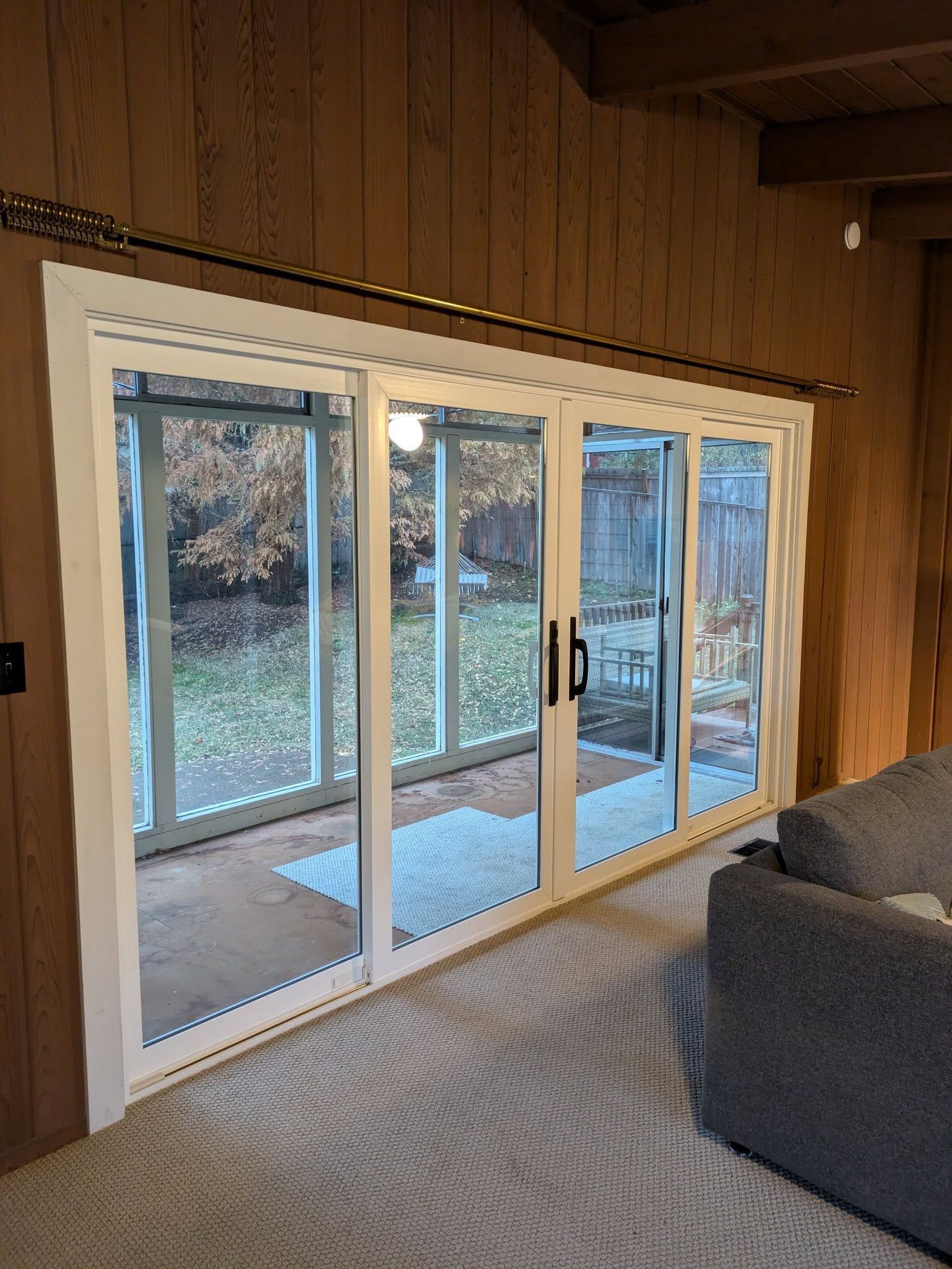 White-framed sliding glass doors open to a backyard. Brown wood paneling surrounds the doors.