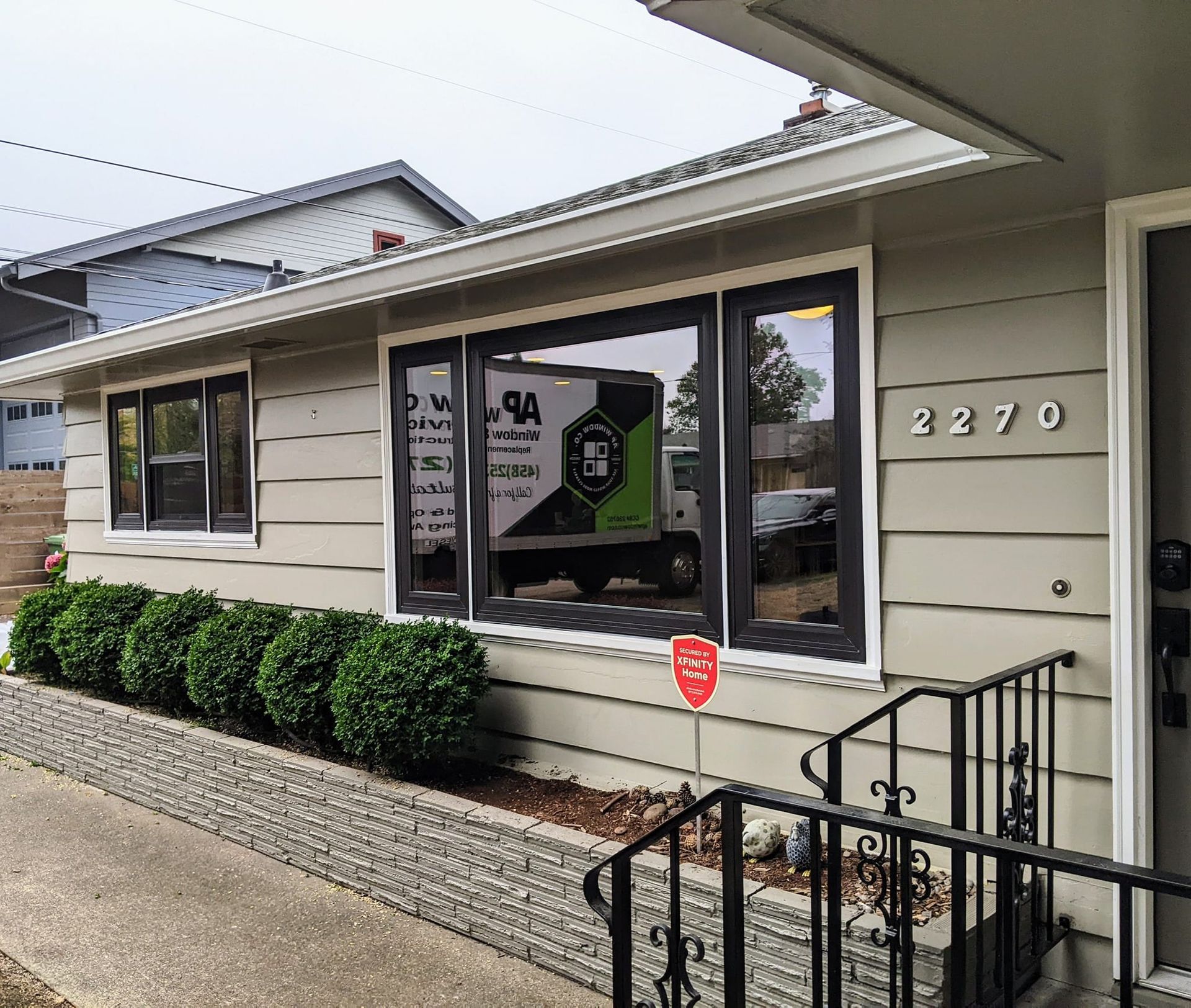 Exterior view of a house with moving truck reflection in windows. Address is 2270, green bushes in front.