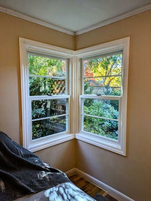 Corner windows with white frames offer a view of a lush green yard; beige walls and white trim.