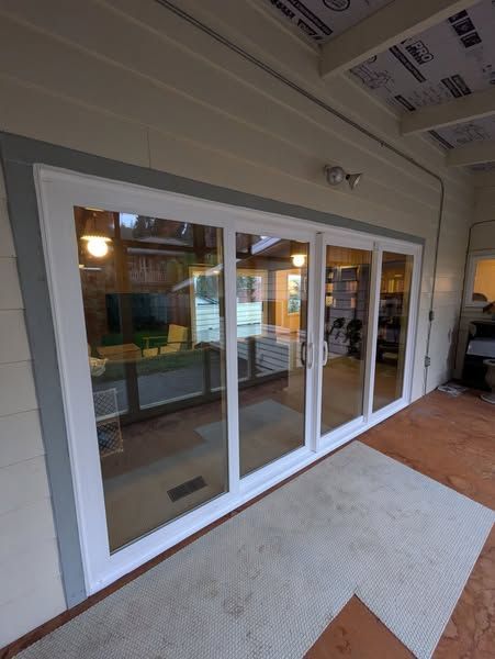 Sliding glass doors with white frames and clear glass. Gray rug on a red-brown patio. Exterior view.