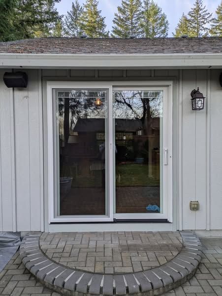 Sliding glass doors with white frame on a light-colored house, brick patio entrance.