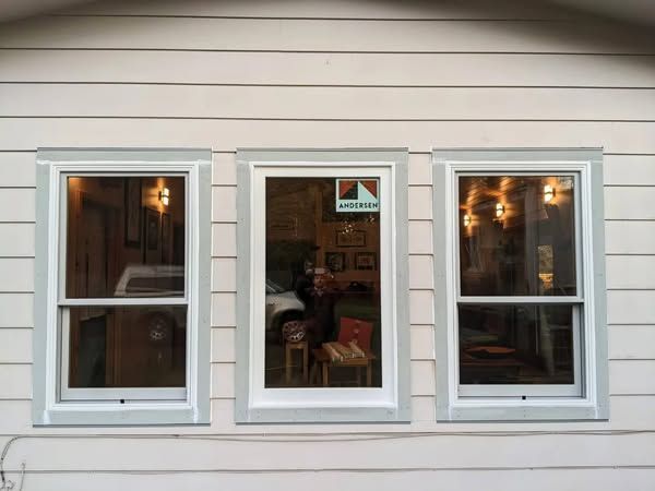 Three white-framed windows with light-blue trim on a light-colored building with horizontal siding.