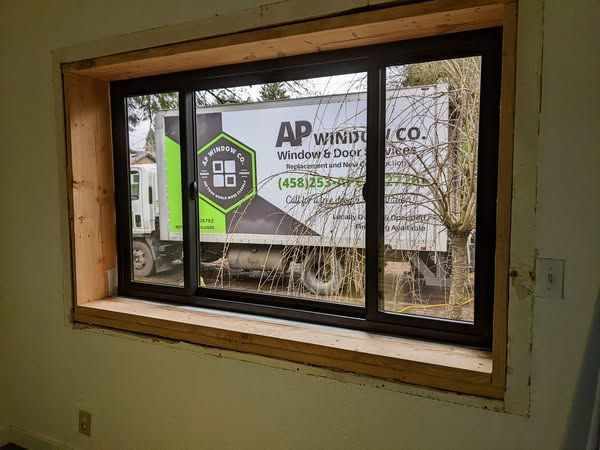 New black framed sliding window in a wooden frame; truck with logo visible through window.