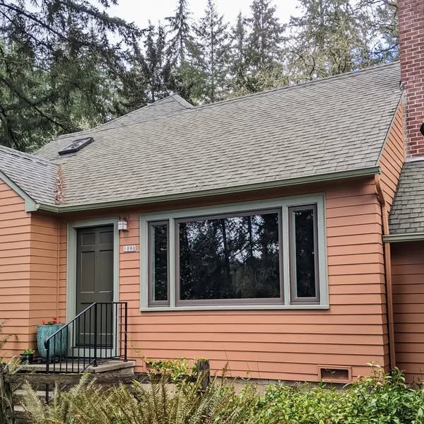 Orange house with green trim, brown door, and shingled roof, set against a forest background.