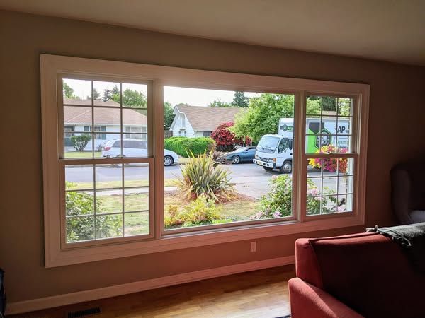 Large window with white trim in a living room, looking onto a street with houses and a parked vehicle.