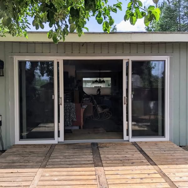 Glass sliding doors with white frames lead into a room. Wooden planks form a deck below.