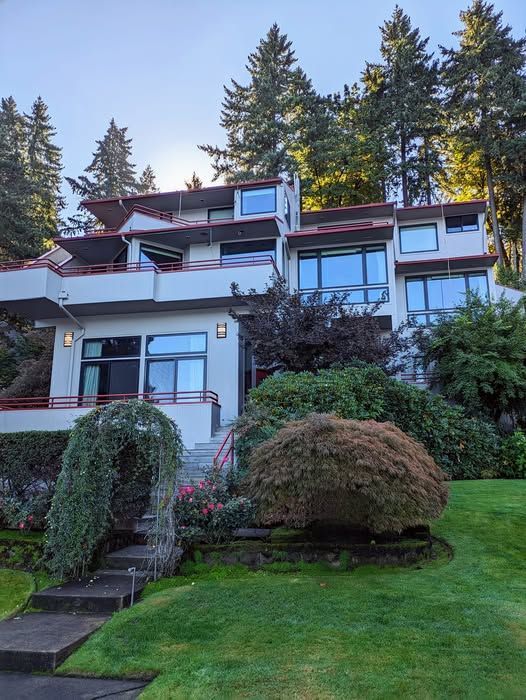 Modern multi-story house on a hillside with red accents, large windows, and lush landscaping.