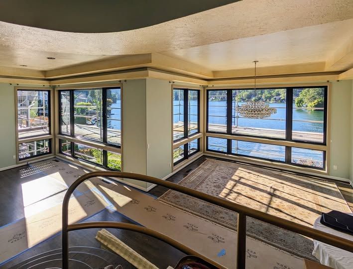 Interior room with large windows overlooking a lake. A chandelier hangs; light shines. Railing in foreground.